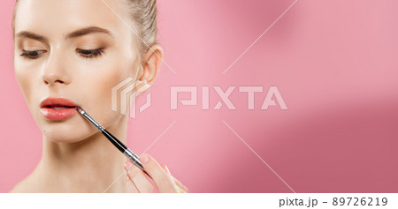 Beauty Concept - Woman applying red lipstick with pink studio background. Beautiful girl makes makeup. Beauty Concept - Woman applying red lipstick with pink studio background. Beautiful girl makes makeup. 89726219