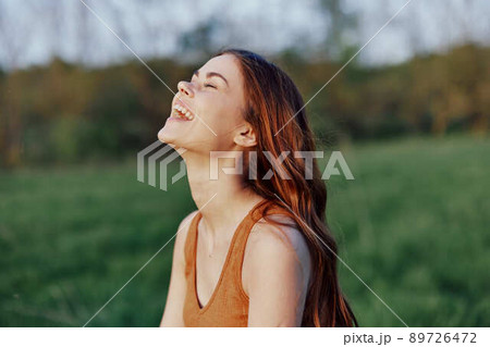 A young woman laughing and smiling merrily in nature in the park with the sunset lighting illuminating her long red hair A young woman laughing and smiling merrily in nature in the park with the sunset lighting illuminating her long red hair 89726472