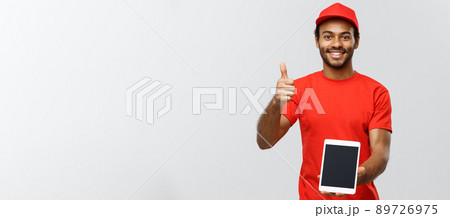 Delivery Concept - Portrait of Handsome African American delivery man or courier showing tablet on you to check the order. Isolated on Grey studio Background. Copy Space. Delivery Concept - Portrait of Handsome African American delivery man or courier showing tablet on you to check the order. Isolated on Grey studio Background. Copy Space. 89726975