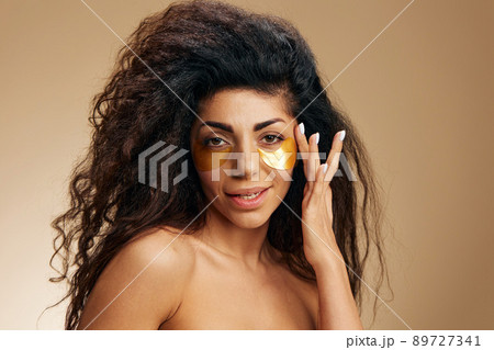 Sexy pretty Latin female apply gold hydrogel patches under eye enjoy flawless facial skin posing isolated over pastel beige background. Cosmetic product ad Natural beauty concept Studio portrait 89727341