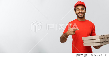 Delivery Concept - Portrait of Happy African American delivery man pointing hand to present pizza box packages. Isolated on Grey studio Background. Copy Space. 89727484