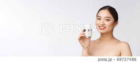 Beautiful young woman on white isolated background holding cosmetic face cream, asian 89727486