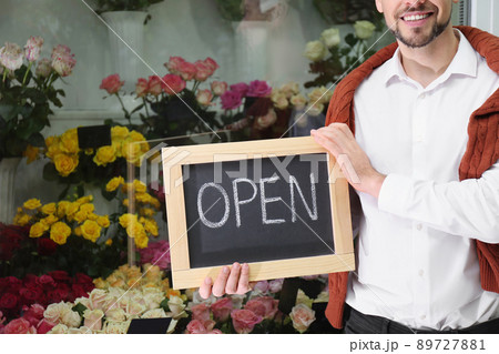 Male business owner holding OPEN sign in his flower shop, closeup Male business owner holding OPEN sign in his flower shop, closeup 89727881