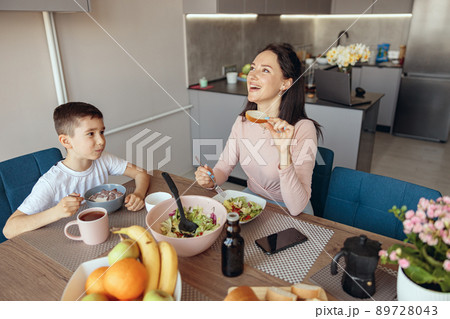 Cheerful mother eating salat in the morning and small son having breakfast with cereals. Cheerful mother eating salat in the morning and small son having breakfast with cereals. 89728043