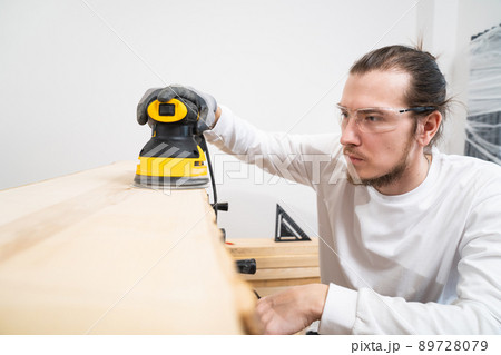carpenter in protective gloves and glasses for working on wood grinding machine carpenter in protective gloves and glasses for working on wood grinding machine 89728079