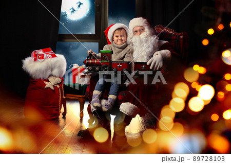 Santa Claus and little boy with toy train near window at home. Christmas holiday 89728103