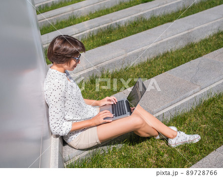 Woman sits with laptop on urban park bench. Freelancer at work. Student learns remotely from outdoors. Modern lifestyle. Summer vibes. Outdoor workplace. Woman sits with laptop on urban park bench. Freelancer at work. Student learns remotely from outdoors. Modern lifestyle. Summer vibes. Outdoor workplace. 89728766