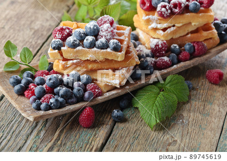 Yummy sweet waffles with raspberries and blueberries on a wooden table . Yummy sweet waffles with raspberries and blueberries on a wooden table . 89745619