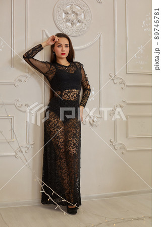 Young beautiful brunette woman in elegant black dress standing near white wall. 89746781