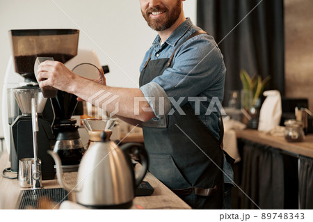 Close up of barista pours coffee beans into the coffee machine tank for grinding at coffeeshop Close up of barista pours coffee beans into the coffee machine tank for grinding at coffeeshop 89748343
