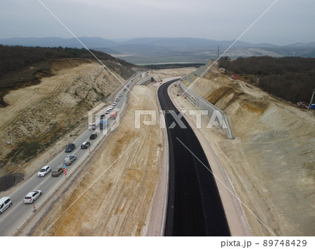 yellow truck pouring bitumen over a new road. Aerial drone shot. Road construction in progress on slope nature canyon. Infrastructure development and logistics. 89748429