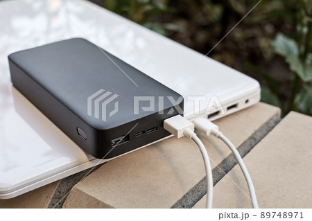 Power bank charges a laptop via USB type C cable on the street. Close-up, selective focus 89748971