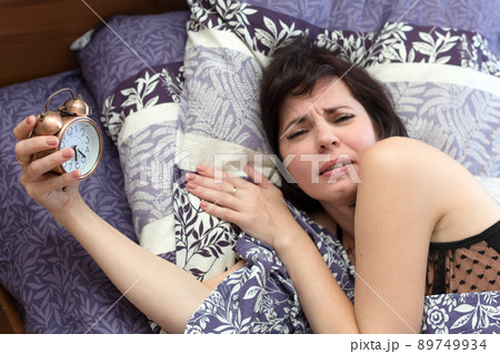 Adult woman wakes up with a headache, gets angry at the ringing alarm clock Adult woman wakes up with a headache, gets angry at the ringing alarm clock 89749934