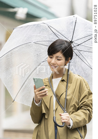 傘をさしてスマートフォンの画面を見る若い女性 89751028