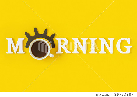 Creative good morning concept. White letters, black eyelashes, alarm clock and cup of coffee on yellow background. Top view, Flat lay. Greeting card 89753387