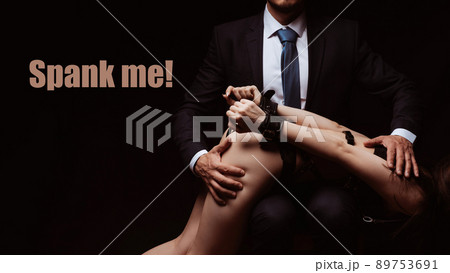 Concept of BDSM sex. Dominant man slaps a submissive girl in leather handcuffs on the ass Concept of BDSM sex. Dominant man slaps a submissive girl in leather handcuffs on the ass 89753691