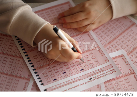Filling out a lottery ticket. A young woman plays the lottery and dreams of winning the jackpot. Female hand marking number on red lottery ticket Filling out a lottery ticket. A young woman plays the lottery and dreams of winning the jackpot. Female hand marking number on red lottery ticket 89754478