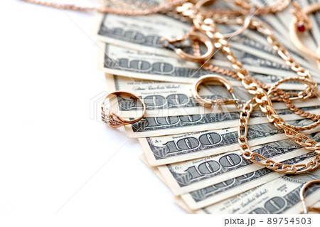 Many expensive golden jewerly rings, earrings and necklaces with big amount of US dollar bills on white background. Pawnshop or jewerly shop Many expensive golden jewerly rings, earrings and necklaces with big amount of US dollar bills on white background. Pawnshop or jewerly shop 89754503
