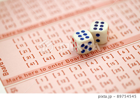 Dice cubes lies on pink gambling sheets with numbers for marking to play lottery. Lottery playing concept or gambling addiction. Close up 89754545