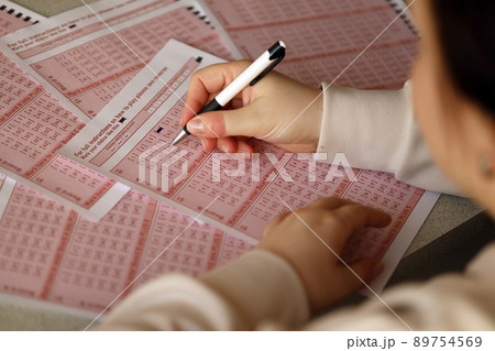 Filling out a lottery ticket. A young woman plays the lottery and dreams of winning the jackpot. Female hand marking number on red lottery ticket 89754569