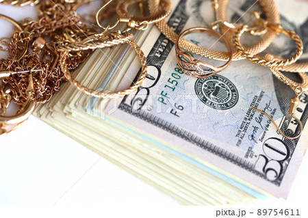 Many expensive golden jewerly rings, earrings and necklaces with big amount of US dollar bills on white background. Pawnshop or jewerly shop 89754611