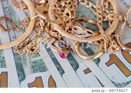 Many expensive golden jewerly rings, earrings and necklaces with big amount of US dollar bills on white background. Pawnshop or jewerly shop Many expensive golden jewerly rings, earrings and necklaces with big amount of US dollar bills on white background. Pawnshop or jewerly shop 89754627