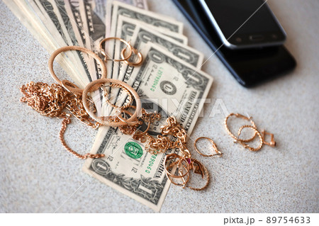 Many expensive golden jewerly rings, earrings and necklaces with big amount of US dollar bills close to smartphones. Pawn shop 89754633