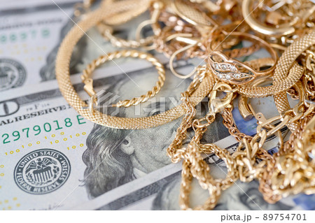 Many expensive golden jewerly rings, earrings and necklaces with big amount of US dollar bills on white background. Pawnshop or jewerly shop Many expensive golden jewerly rings, earrings and necklaces with big amount of US dollar bills on white background. Pawnshop or jewerly shop 89754701