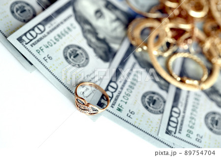 Many expensive golden jewerly rings, earrings and necklaces with big amount of US dollar bills on white background. Pawnshop or jewerly shop Many expensive golden jewerly rings, earrings and necklaces with big amount of US dollar bills on white background. Pawnshop or jewerly shop 89754704