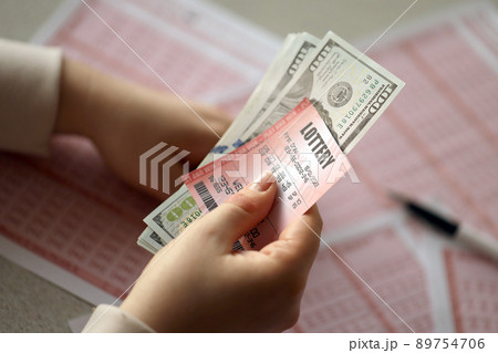 A young woman holds the lottery ticket with complete row of numbers and dollar bills on the lottery blank sheets background 89754706