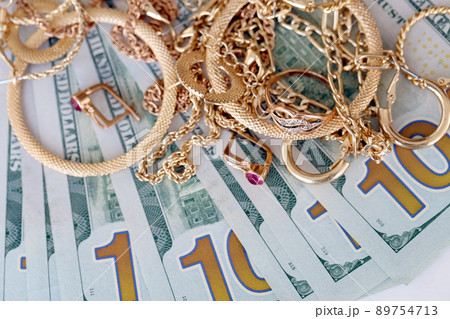 Many expensive golden jewerly rings, earrings and necklaces with big amount of US dollar bills on white background. Pawnshop or jewerly shop Many expensive golden jewerly rings, earrings and necklaces with big amount of US dollar bills on white background. Pawnshop or jewerly shop 89754713