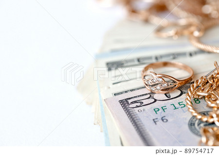 Many expensive golden jewerly rings, earrings and necklaces with big amount of US dollar bills on white background. Pawnshop or jewerly shop 89754717