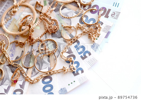 Many expensive golden jewerly rings, earrings and necklaces with big amount of Ukrainian money bills. Pawnshop or jewerly shop concept. Jewelry trading 89754736