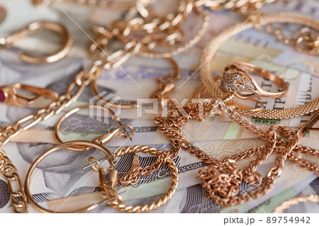 Many expensive golden jewerly rings, earrings and necklaces with big amount of Ukrainian money bills. Pawnshop or jewerly shop concept. Jewelry trading 89754942