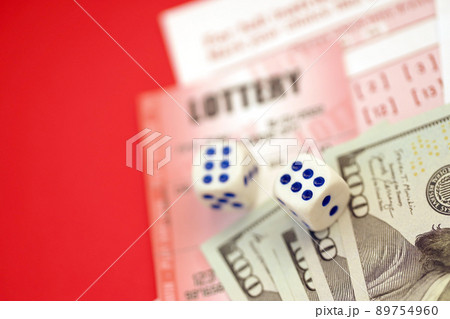 Red lottery ticket with dice and money lies on pink gambling sheets with numbers for marking to play lottery. Lottery playing concept or gambling addiction. Close up Red lottery ticket with dice and money lies on pink gambling sheets with numbers for marking to play lottery. Lottery playing concept or gambling addiction. Close up 89754960