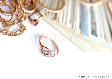 Many expensive golden jewerly rings, earrings and necklaces with big amount of US dollar bills on white background. Pawnshop or jewerly shop 89754971