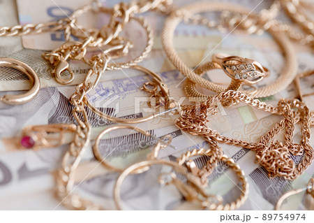 Many expensive golden jewerly rings, earrings and necklaces with big amount of Ukrainian money bills. Pawnshop or jewerly shop concept. Jewelry trading Many expensive golden jewerly rings, earrings and necklaces with big amount of Ukrainian money bills. Pawnshop or jewerly shop concept. Jewelry trading 89754974