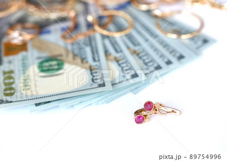 Many expensive golden jewerly rings, earrings and necklaces with big amount of US dollar bills on white background. Pawnshop or jewerly shop Many expensive golden jewerly rings, earrings and necklaces with big amount of US dollar bills on white background. Pawnshop or jewerly shop 89754996