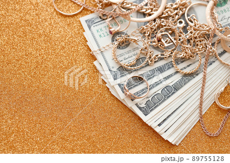 Many expensive golden jewerly rings, earrings and necklaces with big amount of US dollar bills on luxury glitter golden background surface. Pawnshop or jewerly shop Many expensive golden jewerly rings, earrings and necklaces with big amount of US dollar bills on luxury glitter golden background surface. Pawnshop or jewerly shop 89755128