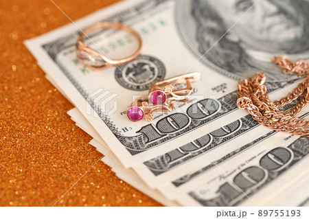 Expensive golden jewerly ring, earrings and necklace with big amount of US dollar bills on luxury glitter golden background surface. Pawnshop or jewerly shop 89755193