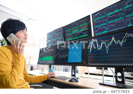 マルチモニターの画面を見ながらスマホで通話する個人投資家　トレーダー　イメージ 89757693