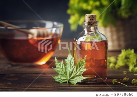 Bottle of maple syrup or healthy tincture and spring maple leaf. Bowl of maple syrup and wooden dipper on background. 89759660