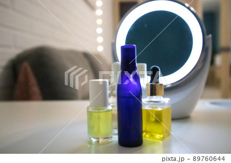 Yellow, blue bottles with natural cosmetics, essential oil, face body skin care aroma oils on white table near еру cosmetic mirror with illumination. Various capacities, limpid glassware. Beauty salon Yellow, blue bottles with natural cosmetics, essential oil, face body skin care aroma oils on white table near еру cosmetic mirror with illumination. Various capacities, limpid glassware. Beauty salon 89760644