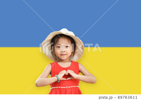 Little girl wear hat showing hands in heart shape on Ukraine flag color background. Stop the war for peace. Love Ukraine concept. Little girl wear hat showing hands in heart shape on Ukraine flag color background. Stop the war for peace. Love Ukraine concept. 89763611