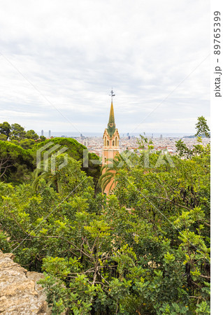 Barcelona, Spain - September 22, 2021: The steeple of the small village in Parc Guell. Park Guell is the famous architectural city art by Antoni Gaudi. Tourist hot spot. Cityscape in the background Barcelona, Spain - September 22, 2021: The steeple of the small village in Parc Guell. Park Guell is the famous architectural city art by Antoni Gaudi. Tourist hot spot. Cityscape in the background 89765399