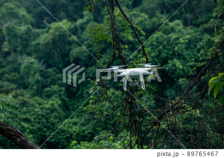 White drone with camera flying in summer forest White drone with camera flying in summer forest 89765467