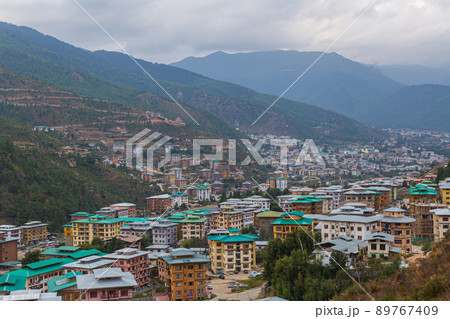 Thimphu, Bhutan - October 26, 2021: Aerial view cityscape of Bhutan capitol city. Top view with dramatic cloudy sky over the town. Largest city in Bhutan in a mountain valley. Houses with green roof Thimphu, Bhutan - October 26, 2021: Aerial view cityscape of Bhutan capitol city. Top view with dramatic cloudy sky over the town. Largest city in Bhutan in a mountain valley. Houses with green roof 89767409