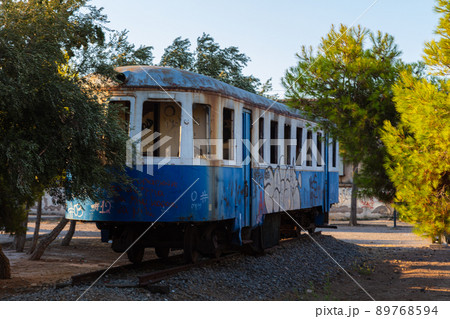 Lavrio, Greece - July 28, 2021: Old tram in a park in Lavrio. Covered in graffiti and without window glass. Discarded tram between trees in a park. Museum piece of former Public transport 89768594