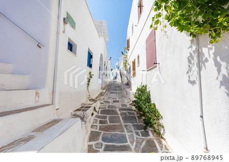 Paros, Greece - August 3, 2021: For the islands of the Cyclades archipelago typical narrow streets with white houses and blue roofs. Marble paved sidewalks. Located in the mediterranean Aegean Sea  89768945