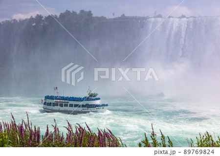 Niagara Falls, Canada - August 27, 2021: The Maid of Mist at the Ontario Side of the Niagara Falls. One of the Tourist attractions at the huge water falls. Tourists getting wet during the boat ride. Niagara Falls, Canada - August 27, 2021: The Maid of Mist at the Ontario Side of the Niagara Falls. One of the Tourist attractions at the huge water falls. Tourists getting wet during the boat ride. 89769824
